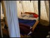 Blick auf ein rekonstruiertes Holzbett in einer hypothetischen Feldlagersituation. Im Hintergrund hängende Tranlampen